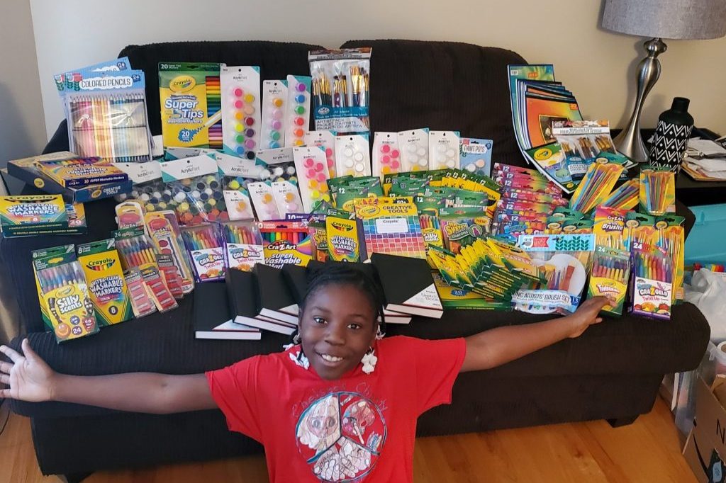 girl with stretched arms posing in front of a table full of art supplies