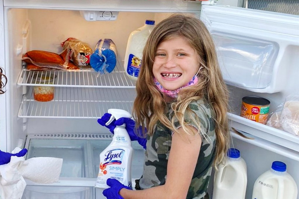 smiling girl holds spray bottle of cleanser near open fridge