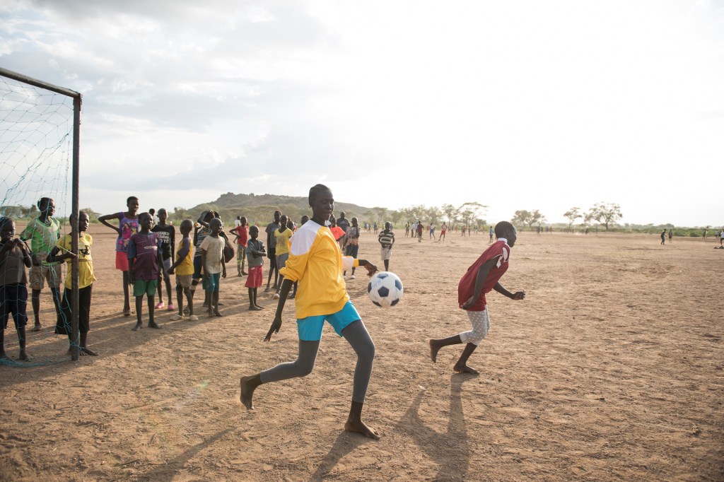 barefoot kids playing soccer on a sandy field