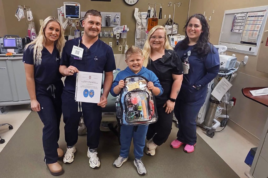 A boy holds a packed bag while posing with four medical workers in a hospital room.
