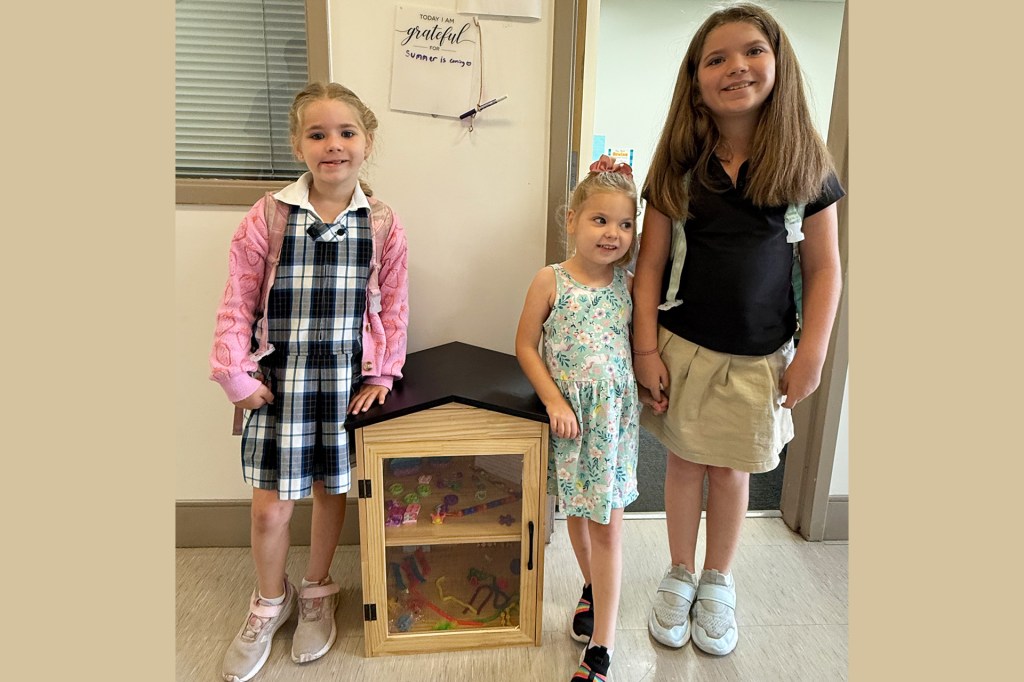 Three smiling girls stand near a small cabinet filled with fidget toys.
