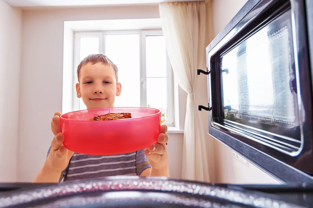 Boy places a bowl of food into a microwave, viewed from the inside of the microwave.
