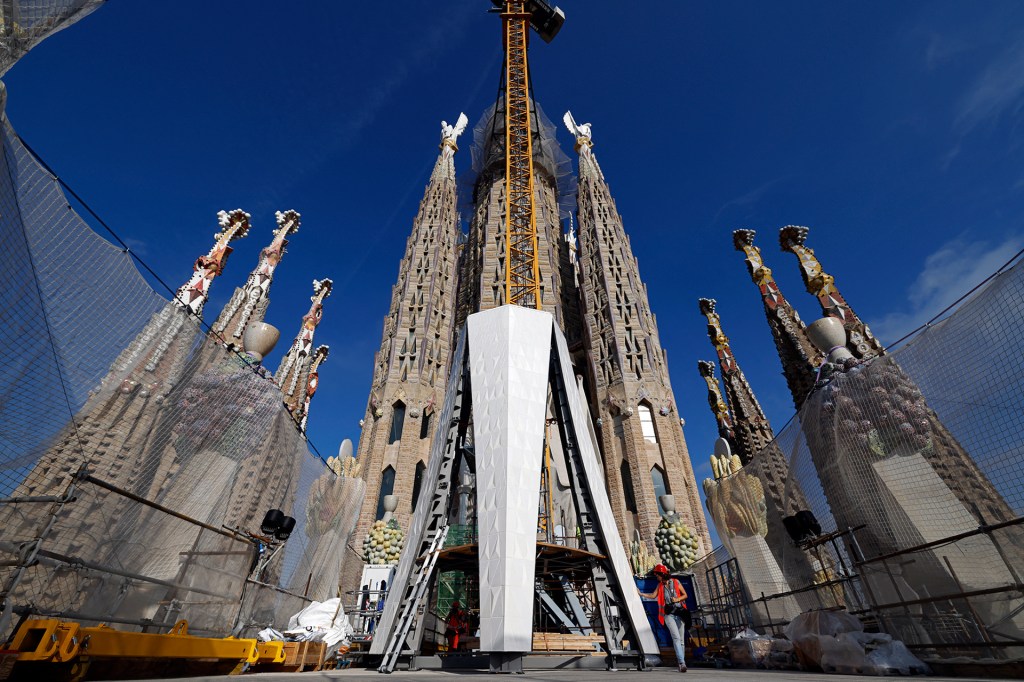 Construction workers and scaffolding surround the tall, detailed towers of the Sagrada Família basilica in Barcelona.