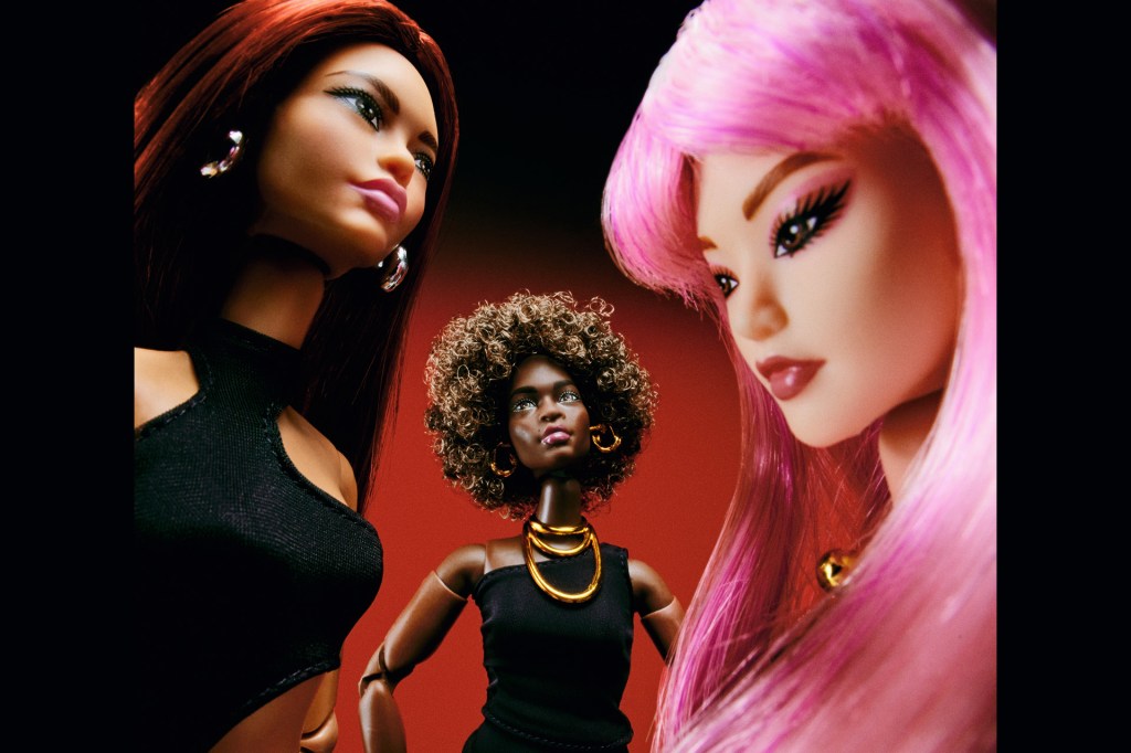 Close-up of three Barbie dolls with different hairstyles and outfits, posed against a red background.