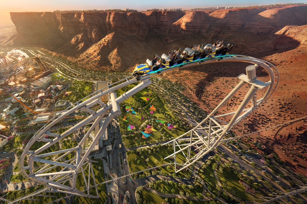 A roller coaster speeds along a high track with riders, overlooking a desert canyon and a colorful amusement park below.
