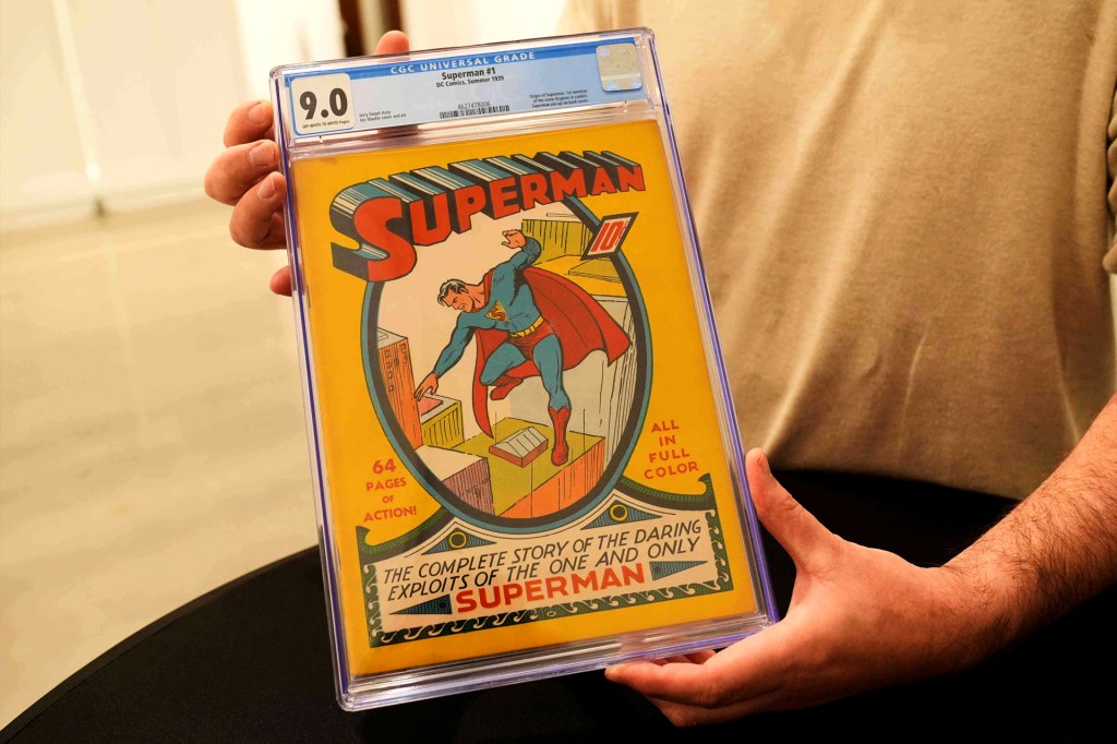 Someone holds a Superman comic in a clear case. The bright yellow cover shows Superman leaping over city rooftops.