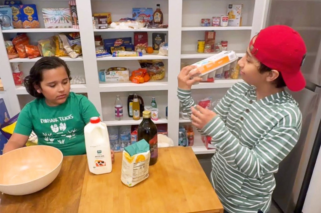 Two kids read a food label in a kitchen pantry.