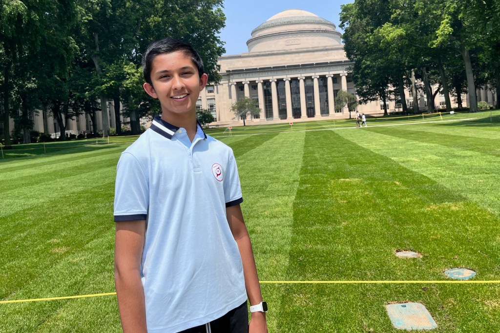 A boy in a blue shirt standing on the lawn of a stone building with columns and a rotunda.