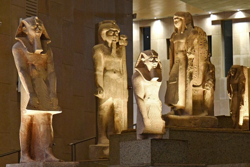 Stone statues of ancient Egyptian kings stand in a museum gallery.