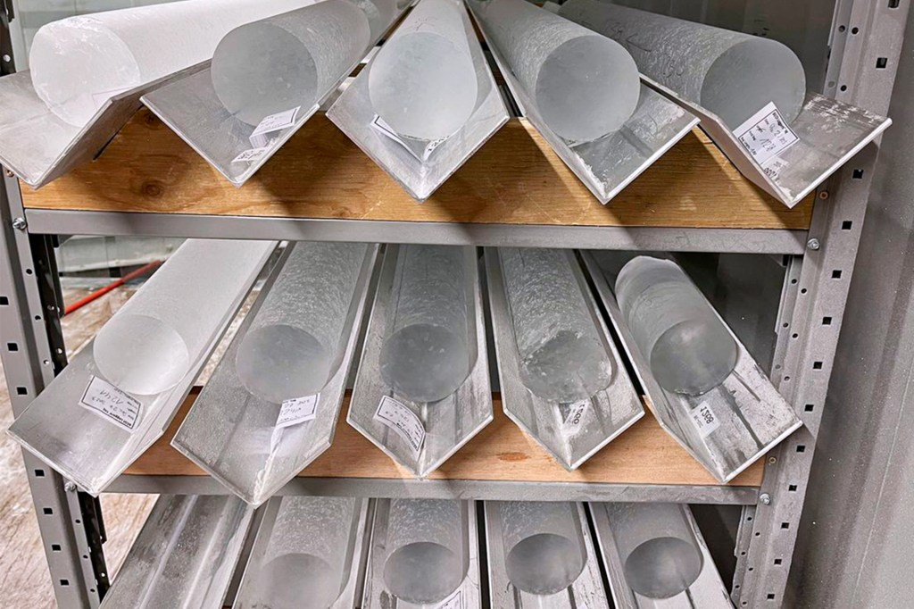 Long cylindrical ice cores are stored on metal shelves inside a cold storage room.