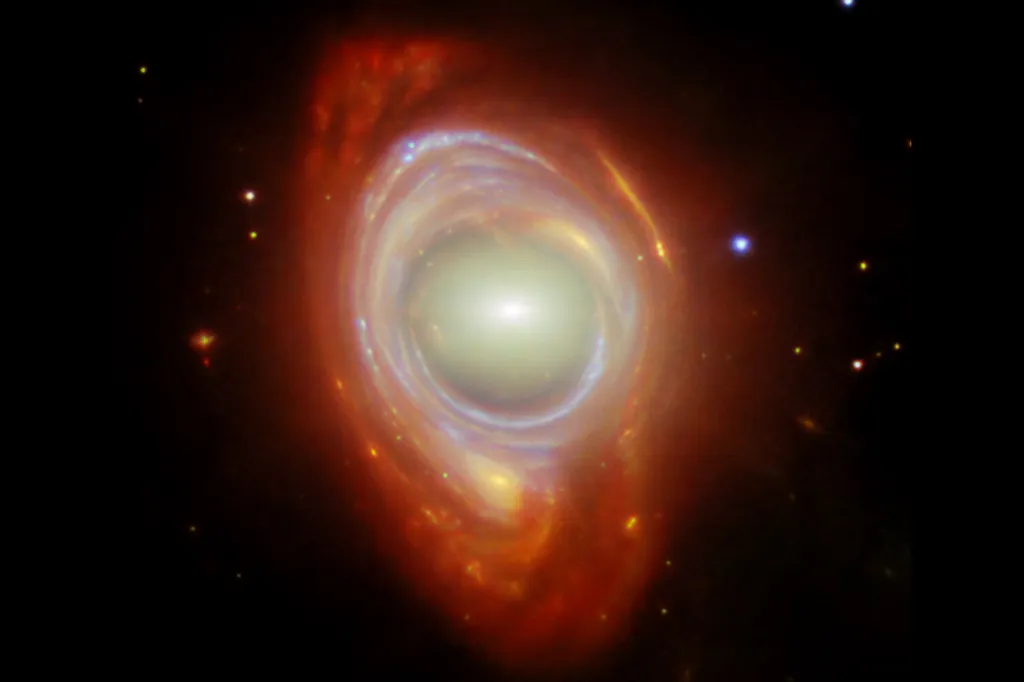 A bright, glowing galaxy with swirling rings of gas and dust surrounds a pale center in deep space.