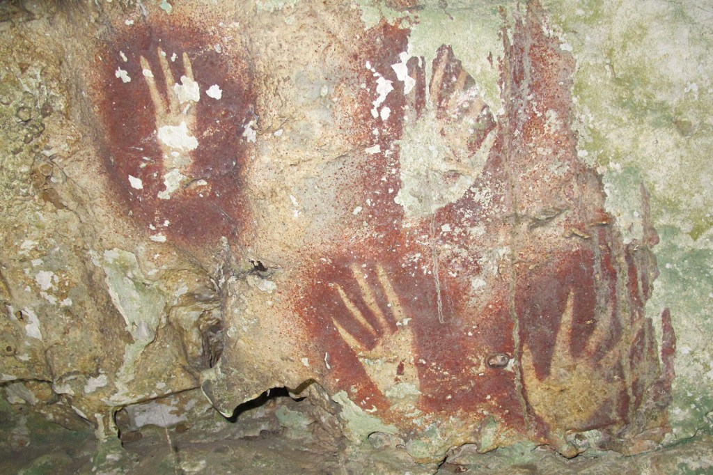 Red handprints painted on a rough cave wall show ancient markings made long ago.