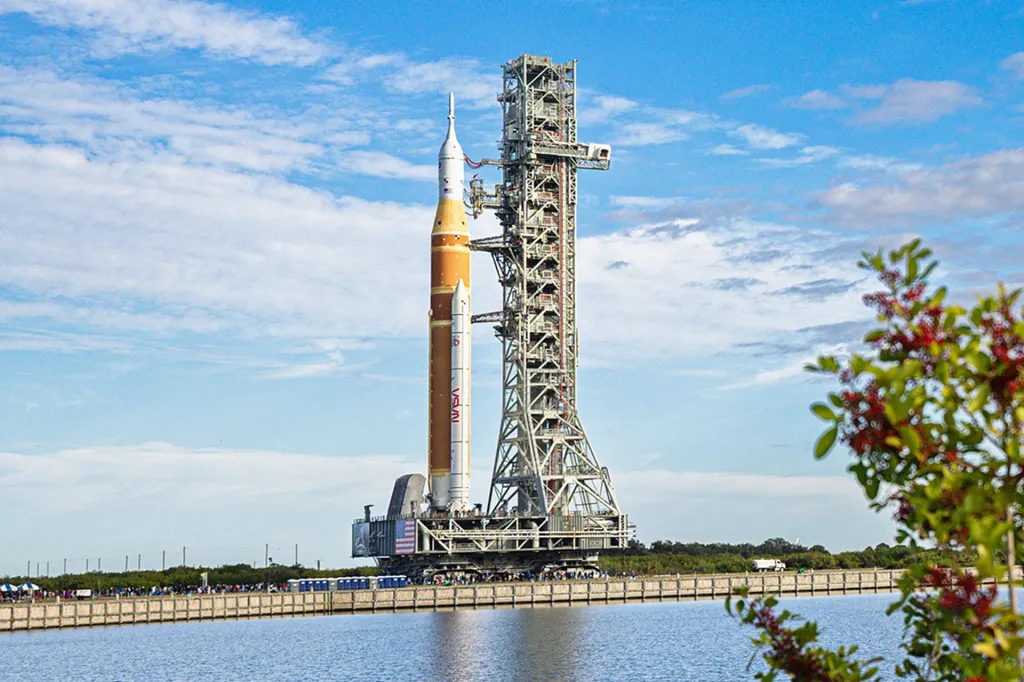 A tall rocket stands upright on a launch pad beside a metal tower under a blue sky.