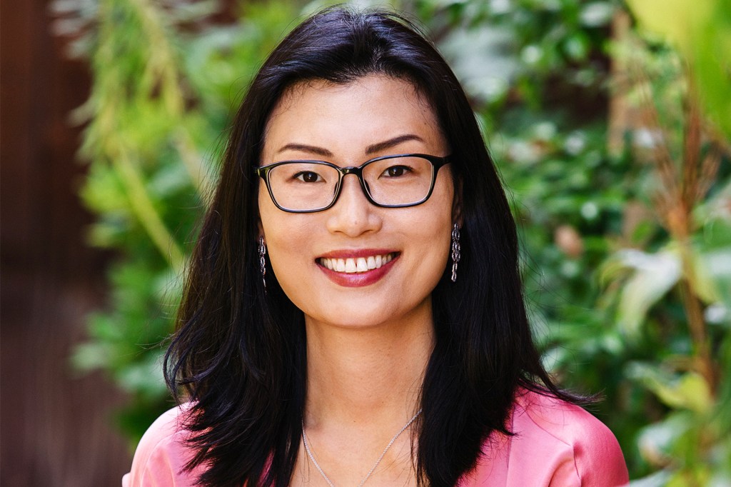 A smiling woman wearing glasses in front of a background of trees.