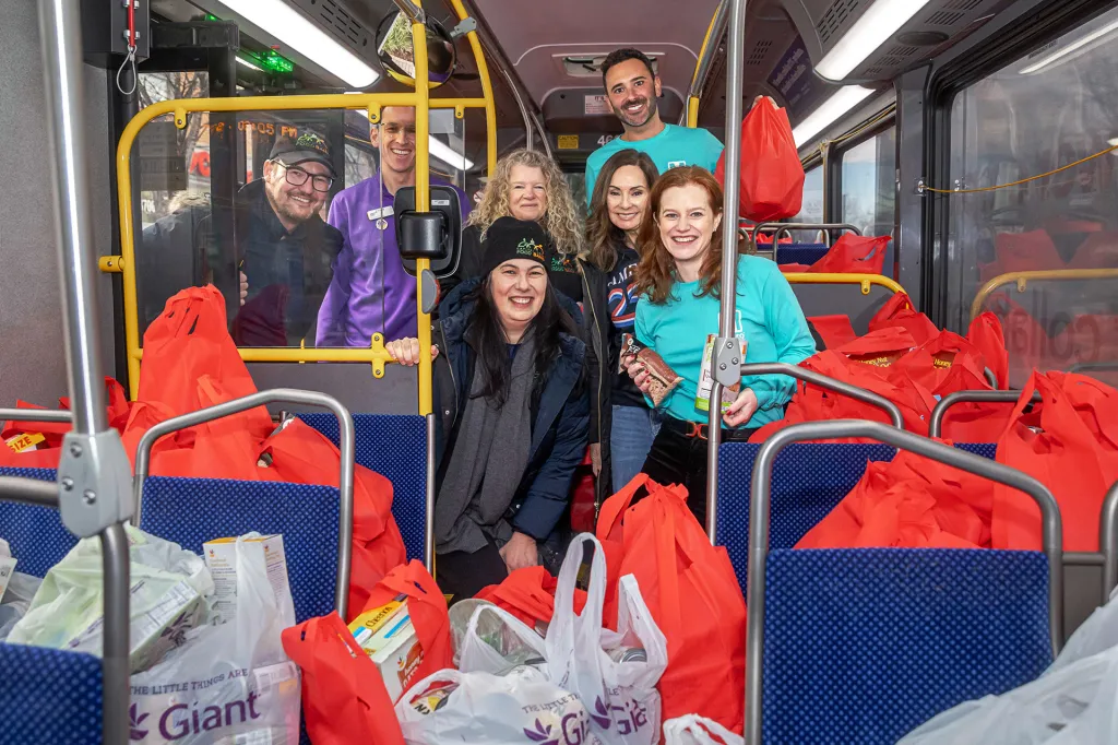 Volunteers stand inside a bus filled with red bags of donated groceries.