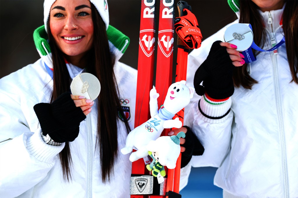 A smiling skier holds a silver medal and a white plush stote.