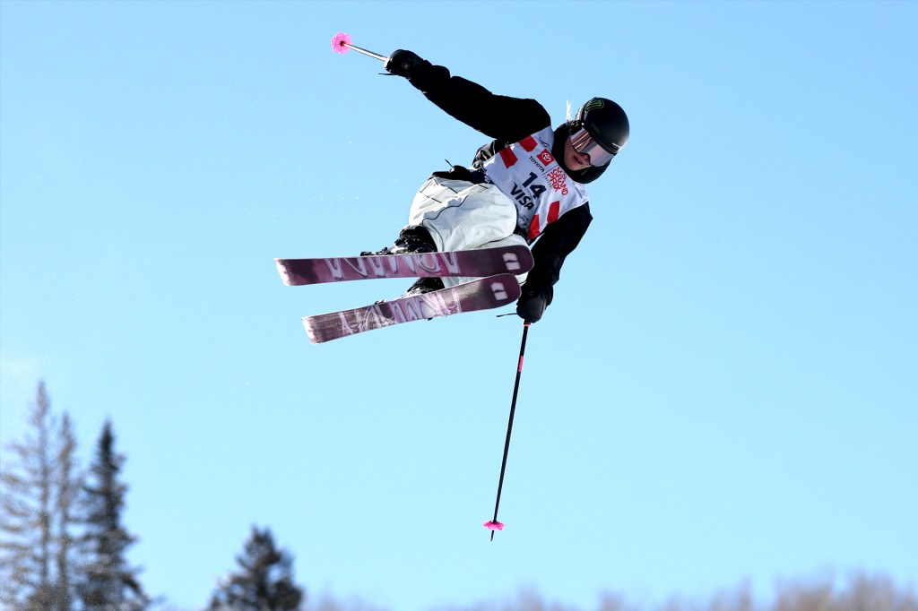 A skier performs a high jump trick in the air against a clear blue sky.