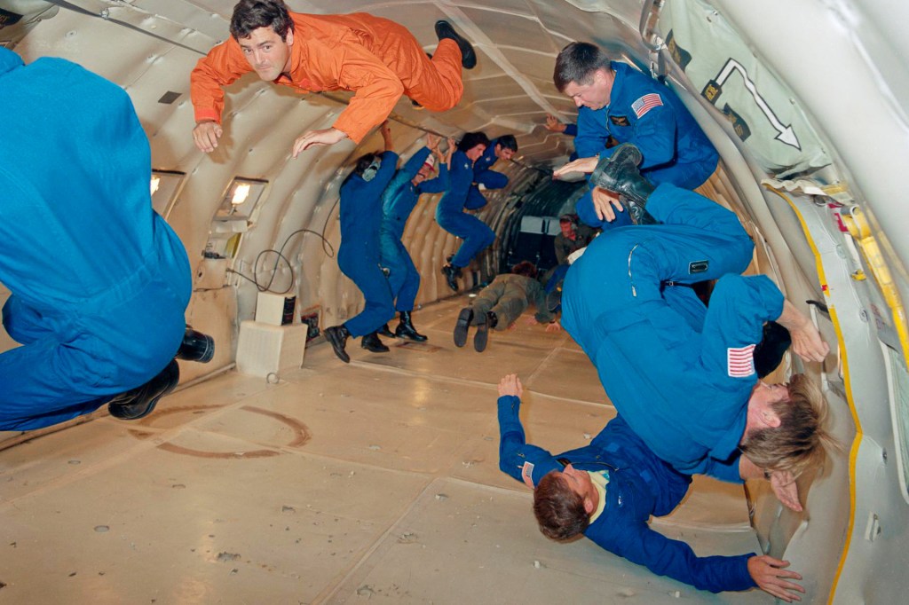 Several people float inside an airplane cabin during a zero-gravity flight, wearing jumpsuits as they practice moving in midair.