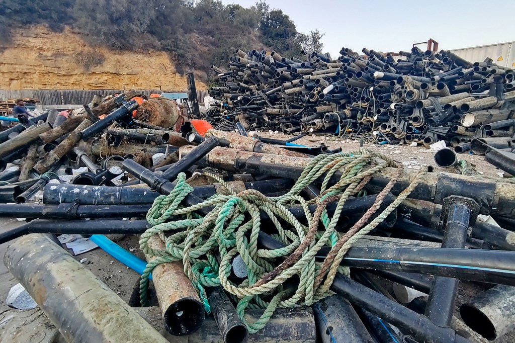 A large pile of old pipes and ropes sits on the ground at a cleanup site near a rocky hillside.