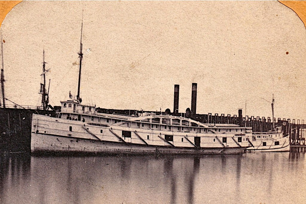 An old black-and-white photograph shows a large steamboat docked along a wooden pier.