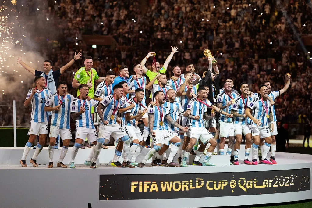 A soccer team celebrates together on a stage, holding a trophy.