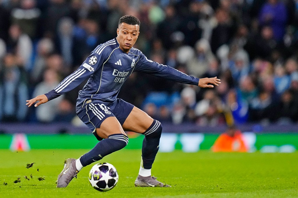 A soccer player in a dark uniform runs and kicks a ball during a game.