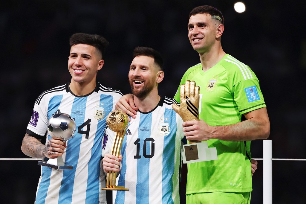 Three soccer players smile and hold trophies and awards after a match.