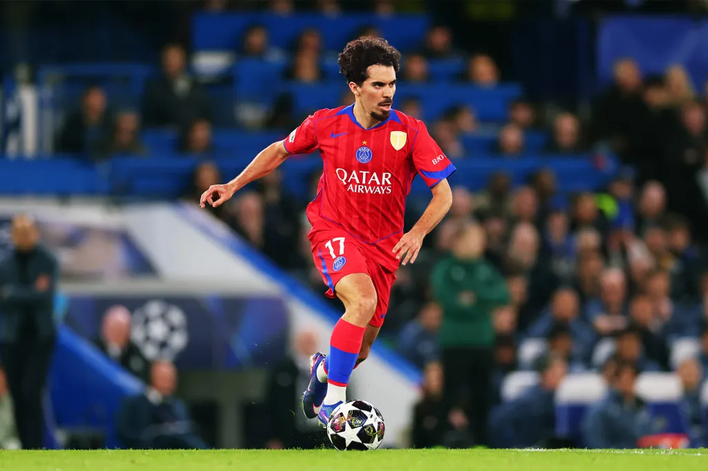 A soccer player in a red uniform dribbles the ball across the field.