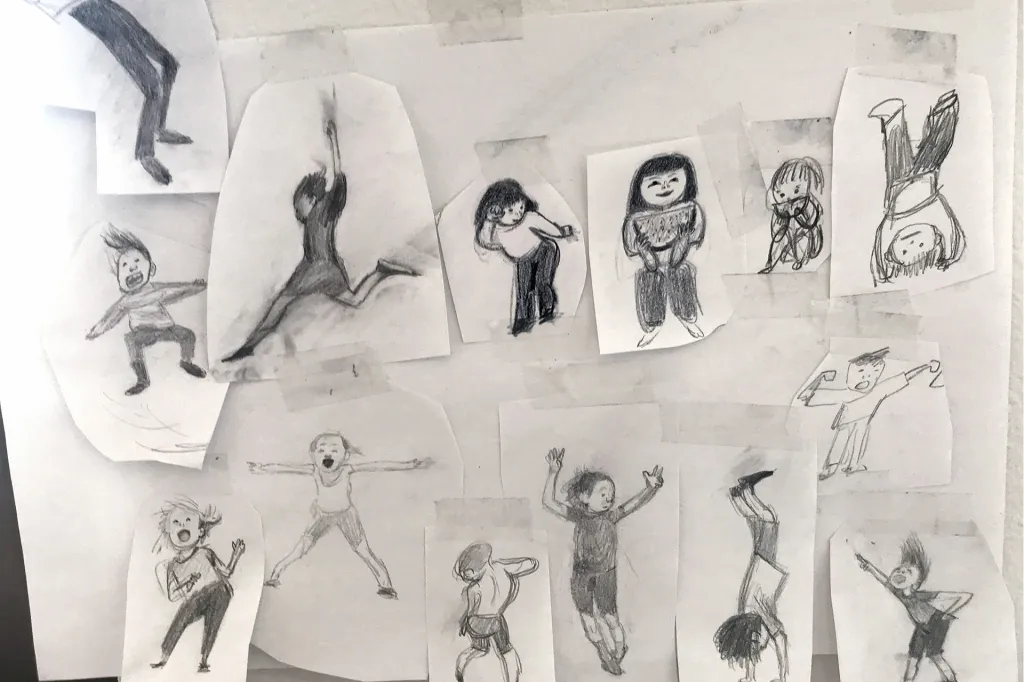 Small drawings of people in different poses are taped to a wall, showing early character sketches.