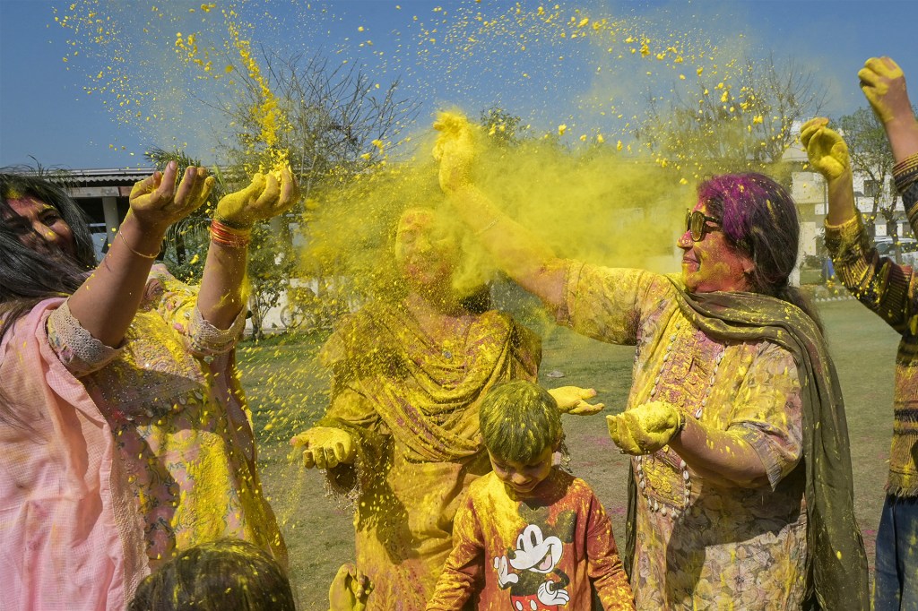 People outdoors throw bright yellow powder into the air and smile as they celebrate together.