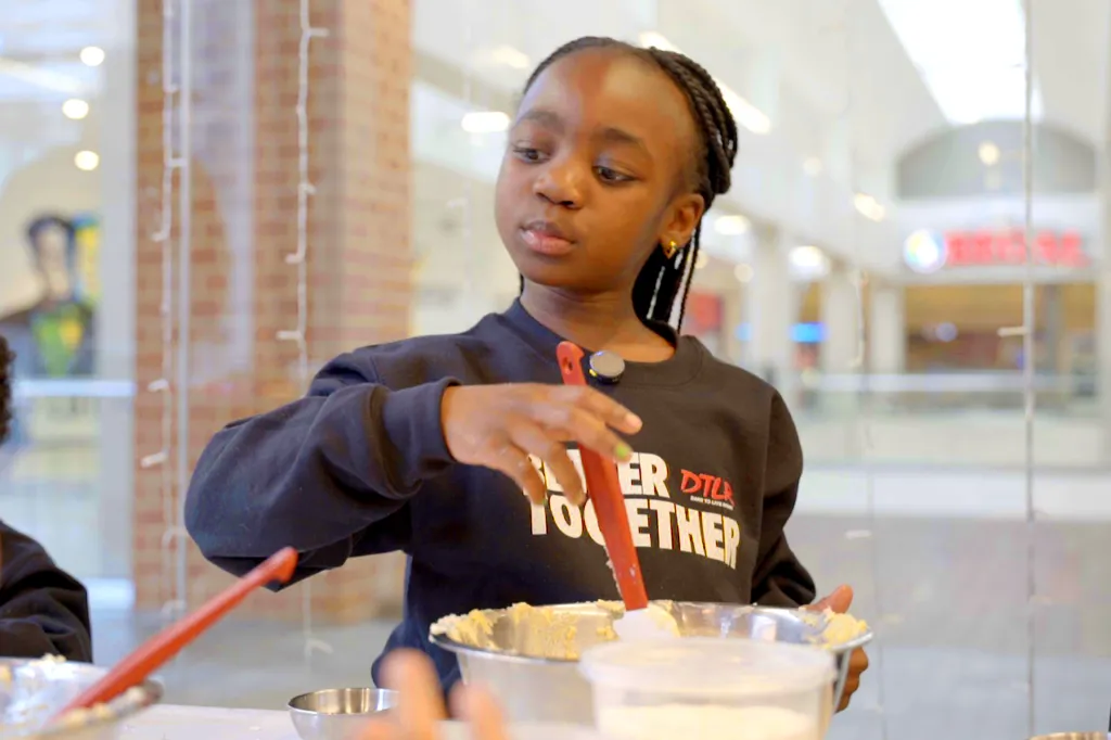 A young girl mixes a batter in a large bowl with a spatula.