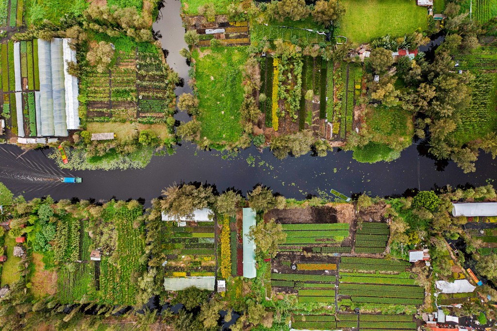 An aerial view of farmed fields along a stream with a barge floating down it.