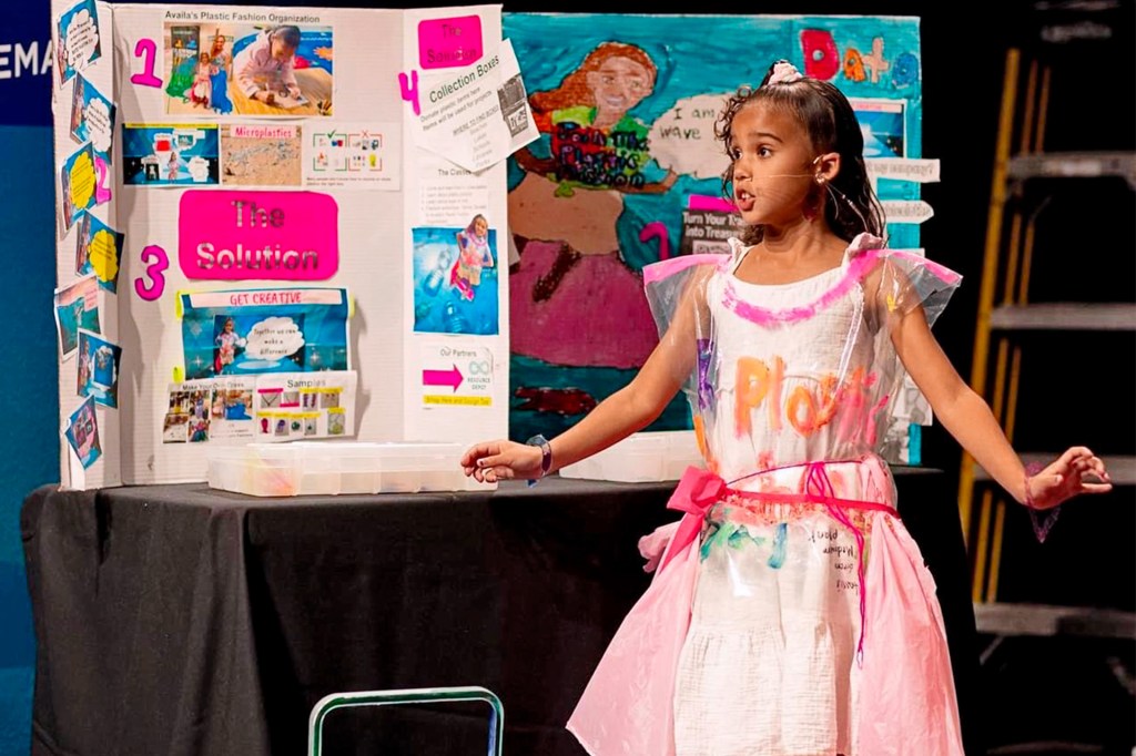 A girl presents a project about plastic and recycling while wearing a dress made from plastic materials.