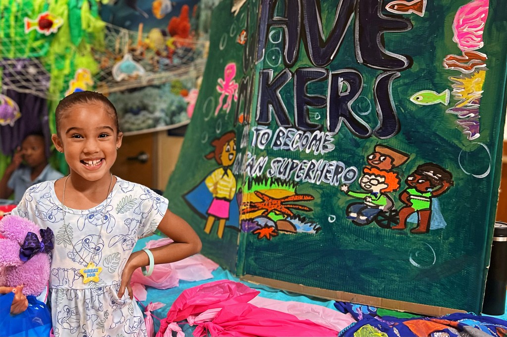 A smiling girl stands next to a colorful display.