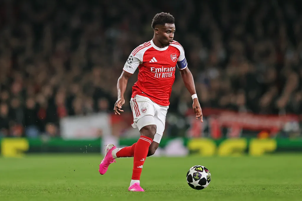 A soccer player in a red and white uniform runs across the field while controlling the ball during a game.