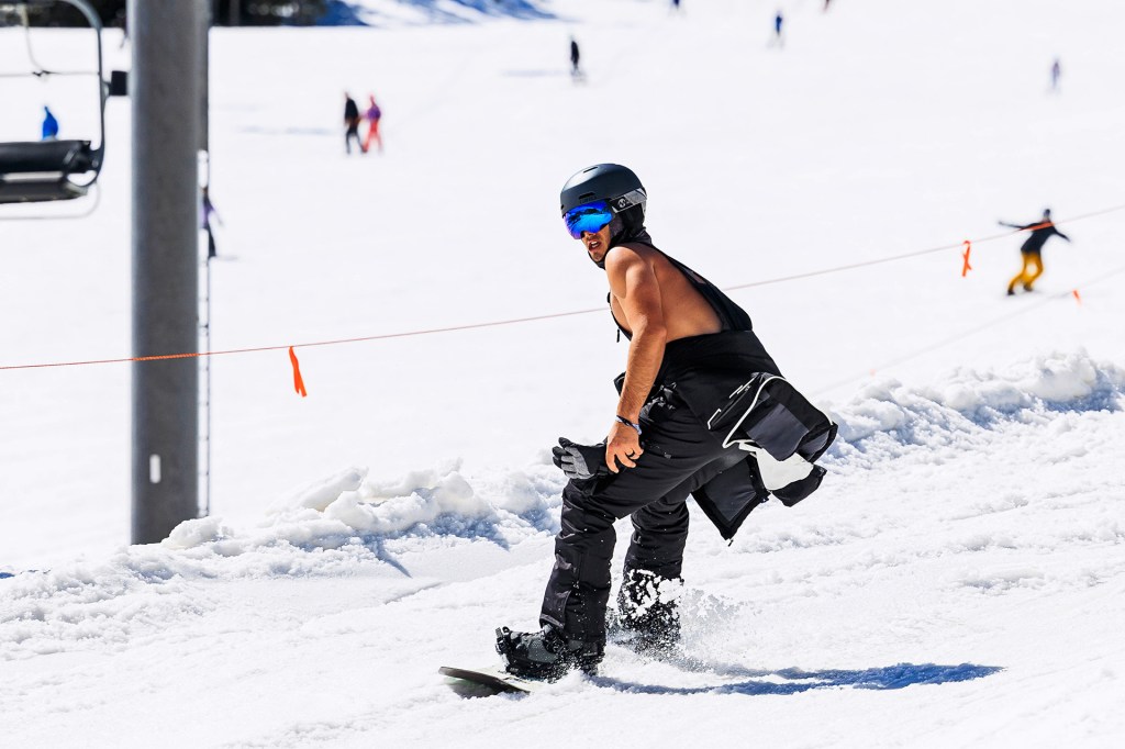 A snowboarder wearing a helmet rides down a snowy slope with other people in the distance.