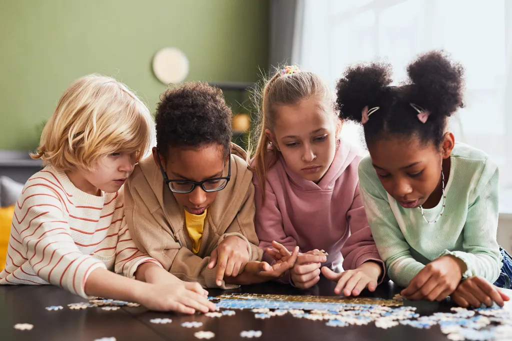 A group of four kids sitting at a table working on a jigsaw puzzle together