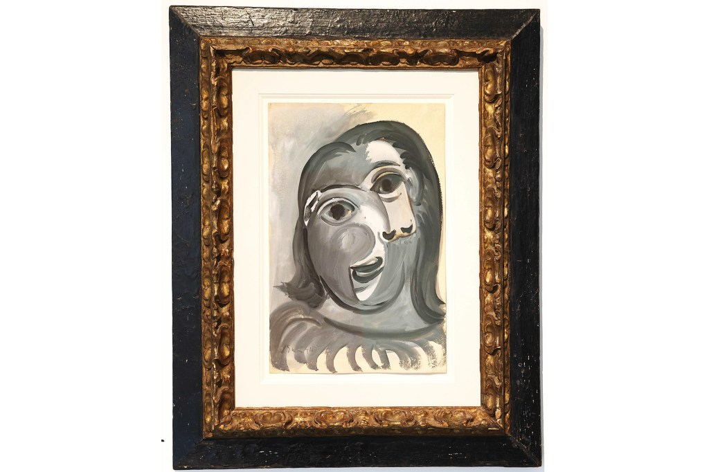A framed black-and-white painting of a person’s face hangs on a wall.