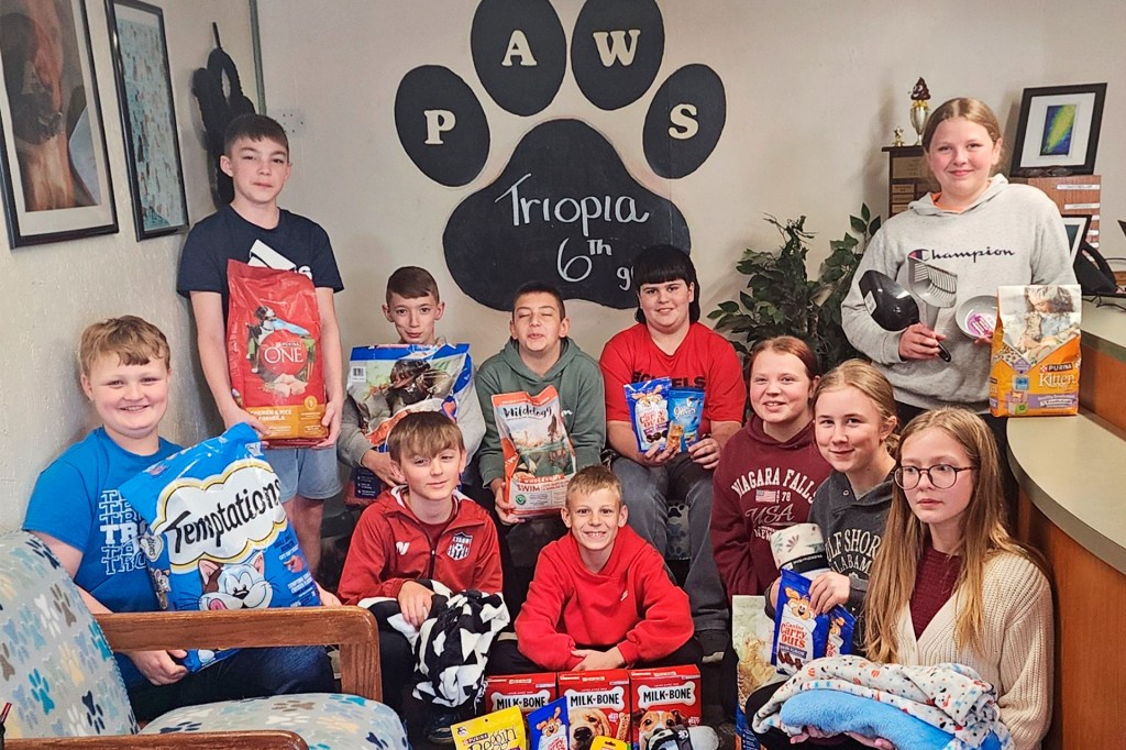 A group of kids pose indoors with donated pet food and supplies.