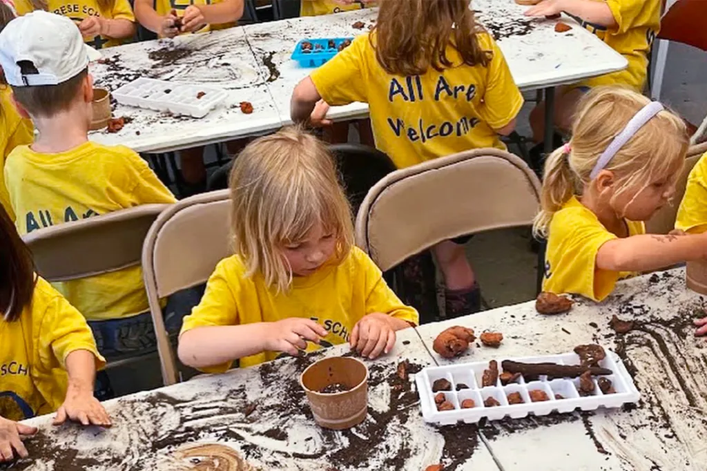 Young children sit at tables, playing with soil and small pots during a hands-on activity.