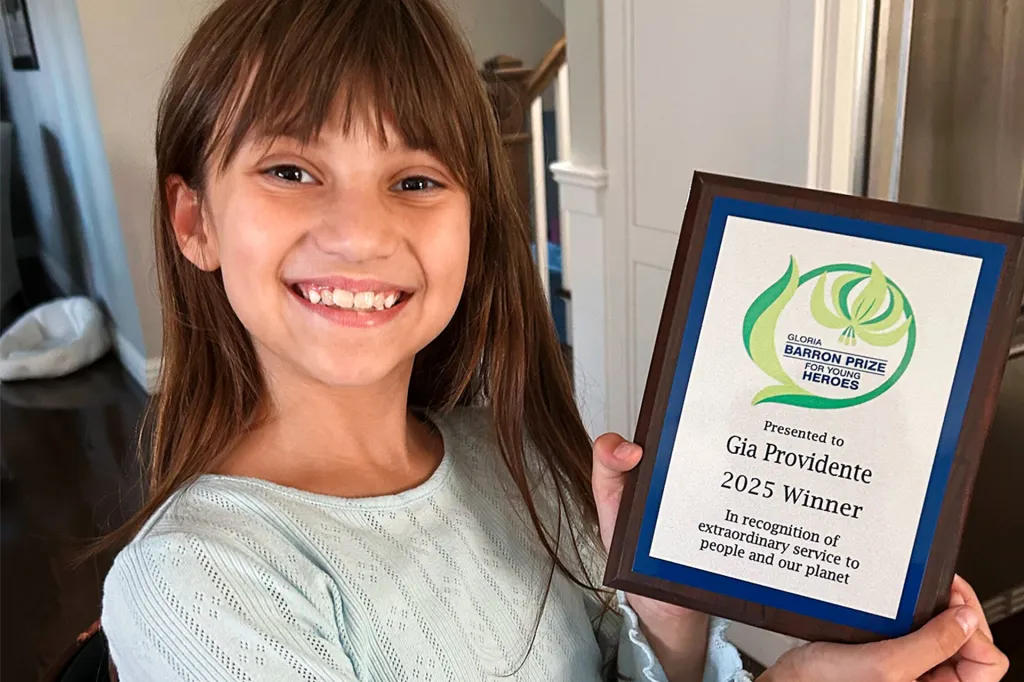 A smiling girl holds a framed award certificate in her hands.