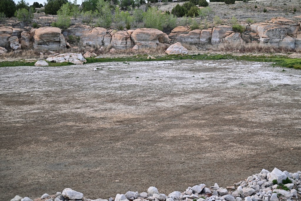 Dry resevoir surrounded by rocks and dry brush in a desert landscape.