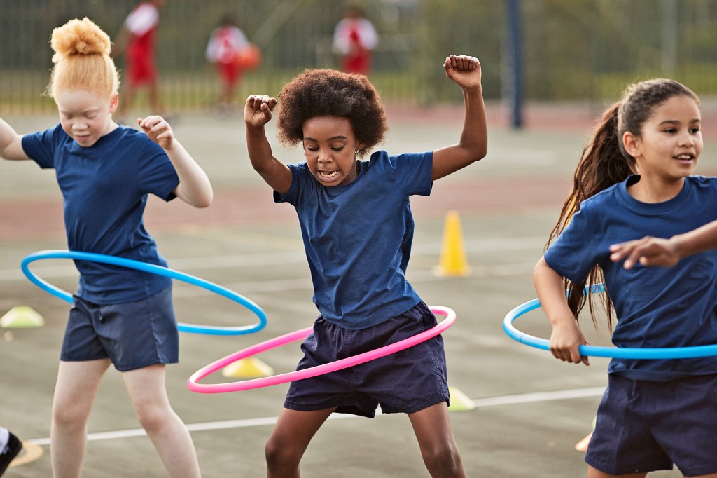Children in blue gym clothes play with hula hoops on an outdoor court.