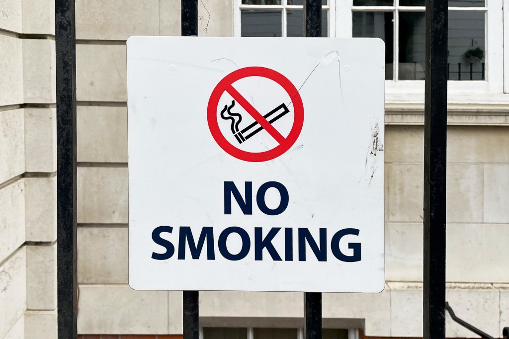 “No Smoking” sign attached to a black metal fence.