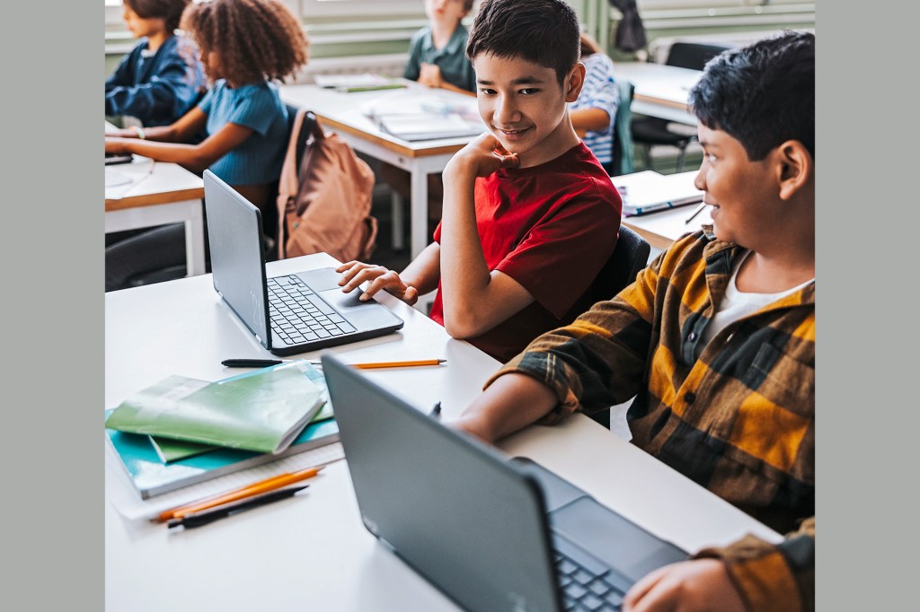 Two students in a classroom with laptop computers on their desks.
