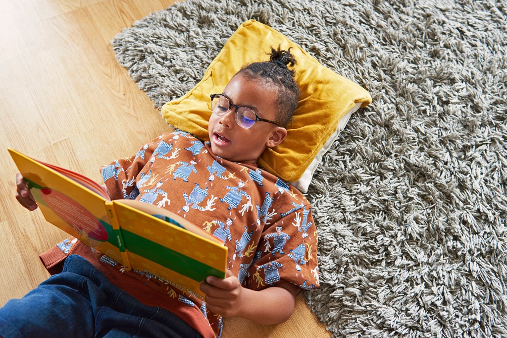 A kid lies on a shaggy rug reading a book.