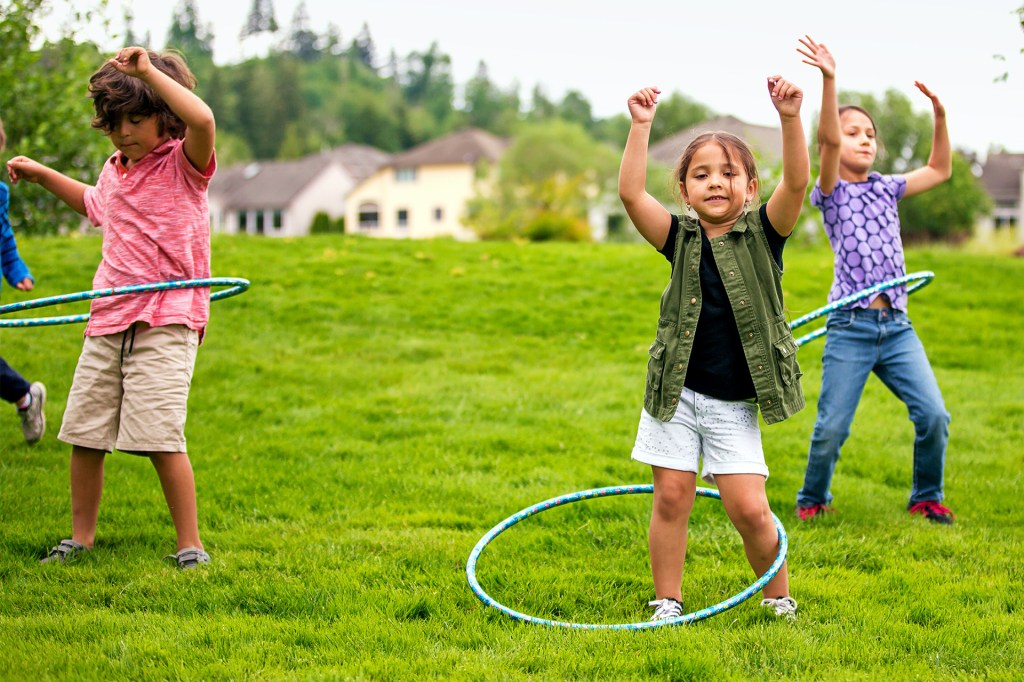 Children play with hula hoops on a grassy field.