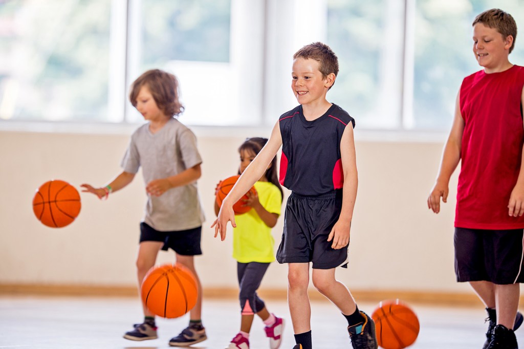 Children dribble basketballs while practicing together in a gym.