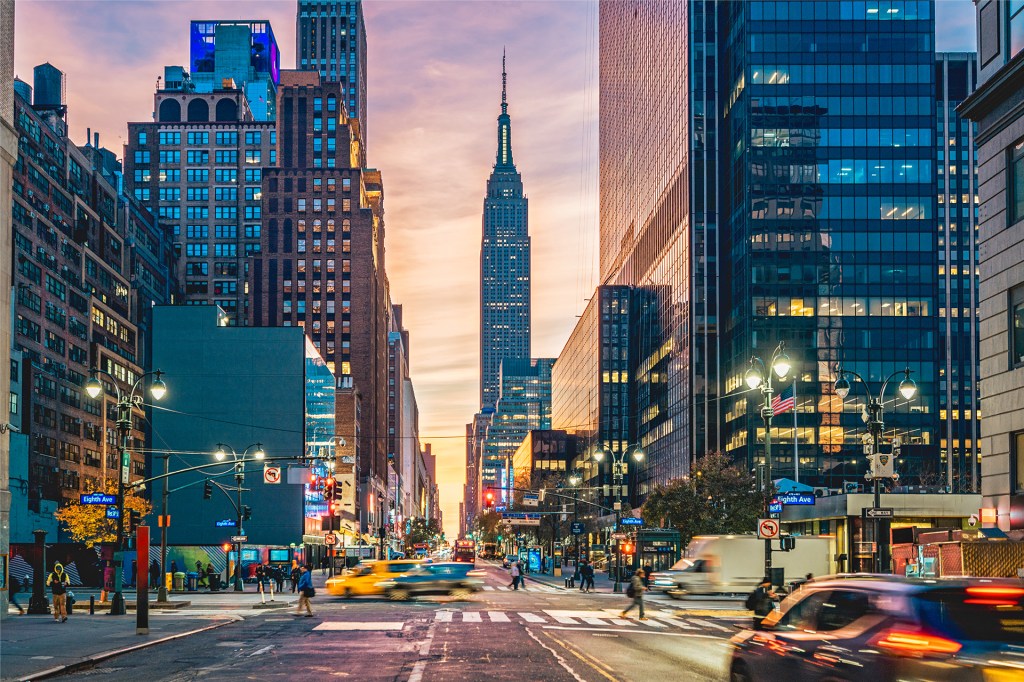 Tall buildings, busy streets, cars, and people fill a city neighborhood.