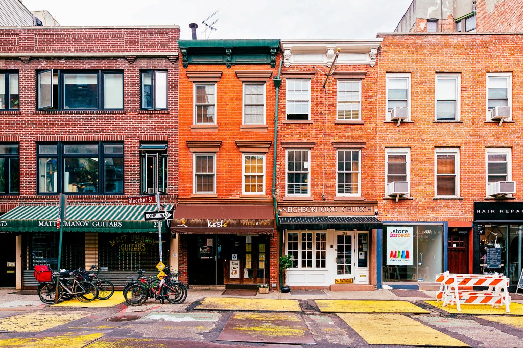Brick buildings with shops, a church, and apartments line a city street.